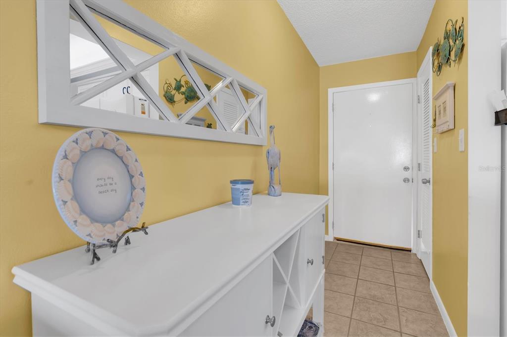 A yellow-walled entryway features a white console table, a decorative mirror, and a tiled floor — 285 107TH AVENUE UNIT 701, TREASURE ISLAND, FL