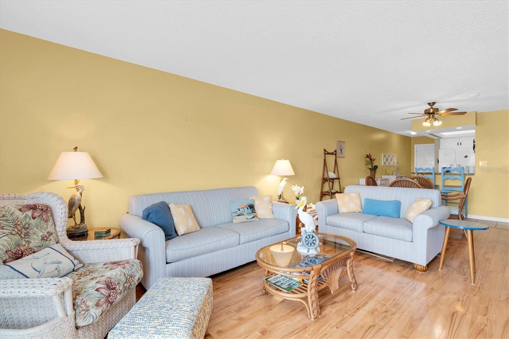 A living room features light blue sofas, a wicker armchair, and a glass-topped coffee table — 285 107TH AVENUE UNIT 701, TREASURE ISLAND, FL