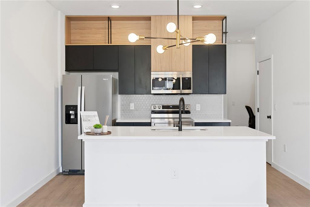 A modern kitchen features black and wood-toned cabinetry, a white island, and a geometric chandelier — 3261 TRANQUIL TRAIL, KISSIMMEE, FL