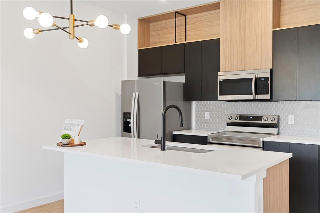 A modern kitchen features a white island, black cabinetry, wood accents, and stainless steel appliances — 3261 TRANQUIL TRAIL, KISSIMMEE, FL