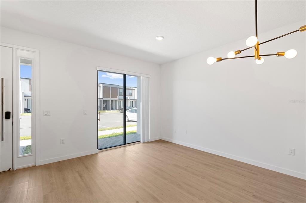 An empty room features light wood-look flooring, white walls, a modern chandelier, and sliding doors — 3261 TRANQUIL TRAIL, KISSIMMEE, FL