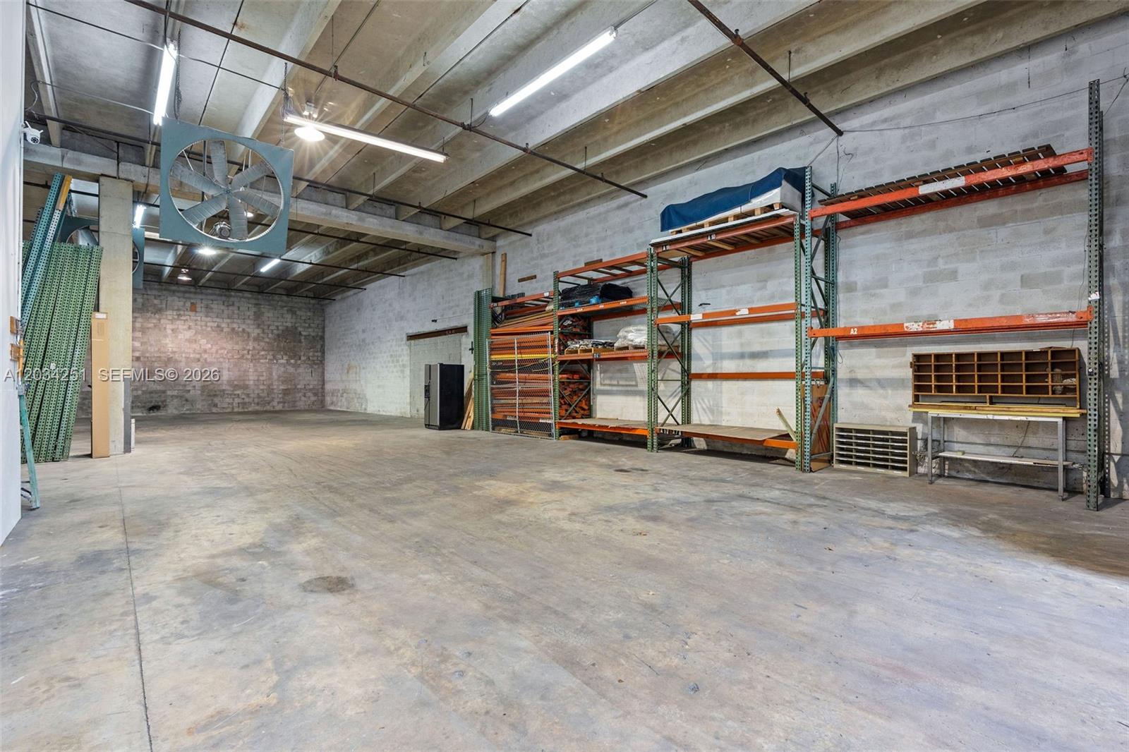 This warehouse space features concrete floors, exposed ceiling beams, industrial shelving, and a large wall fan — 3000 NW 79th Ave # 3000, Doral FL 33122, DORAL, FL