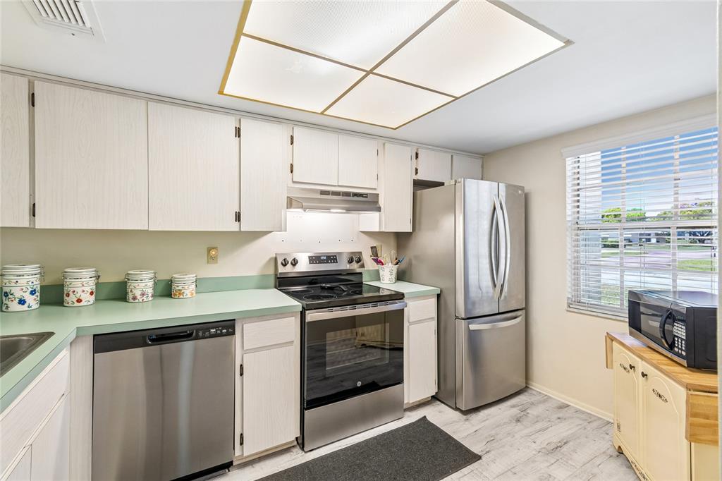 A kitchen with light-colored cabinets, green countertops, stainless steel appliances, and a large ceiling light — 11340 CARRIAGE HILL DRIVE UNIT 4, PORT RICHEY, FL