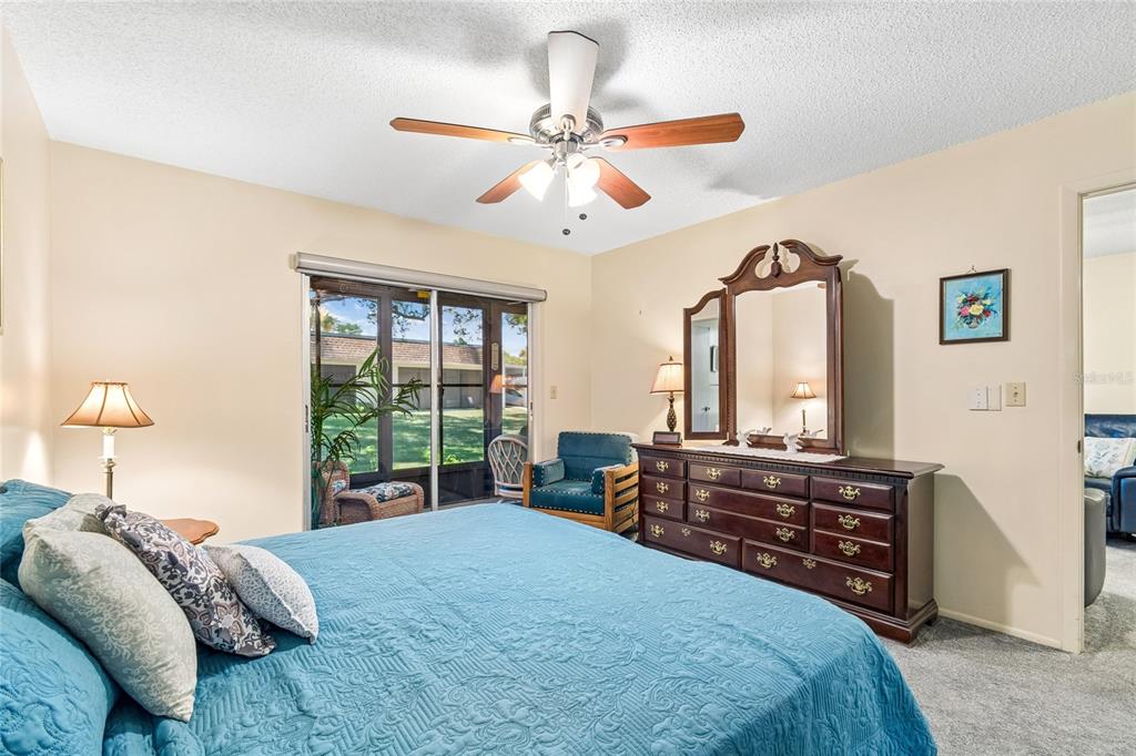 A bedroom features a blue quilt, a wooden dresser with a mirror, and sliding glass doors — 11340 CARRIAGE HILL DRIVE UNIT 4, PORT RICHEY, FL