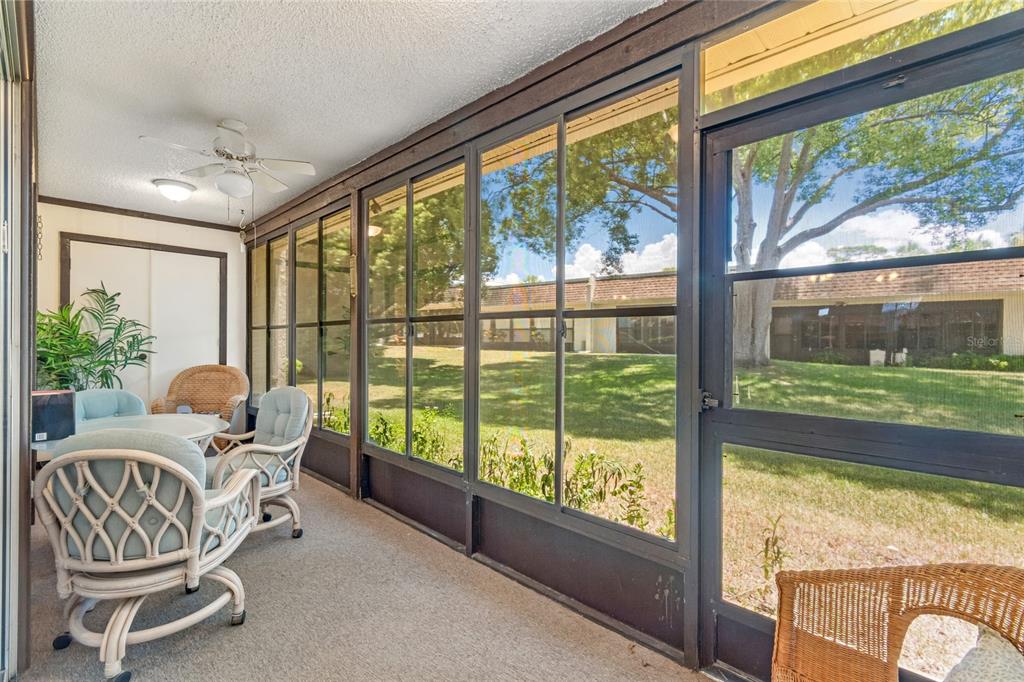 A screened-in porch with wicker furniture, carpeted flooring, and a view of a grassy yard — 11340 CARRIAGE HILL DRIVE UNIT 4, PORT RICHEY, FL