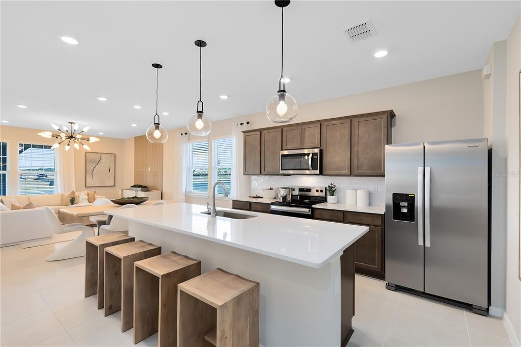 A modern kitchen features a white quartz island, wooden stools, and dark cabinetry — 10674 EVENING STAR STREET, ORLANDO, FL