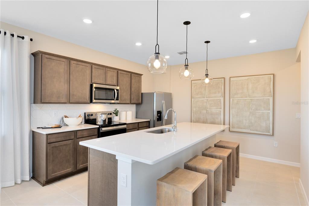 A kitchen features wood cabinets, a white quartz island with bar seating, and pendant lighting — 10674 EVENING STAR STREET, ORLANDO, FL