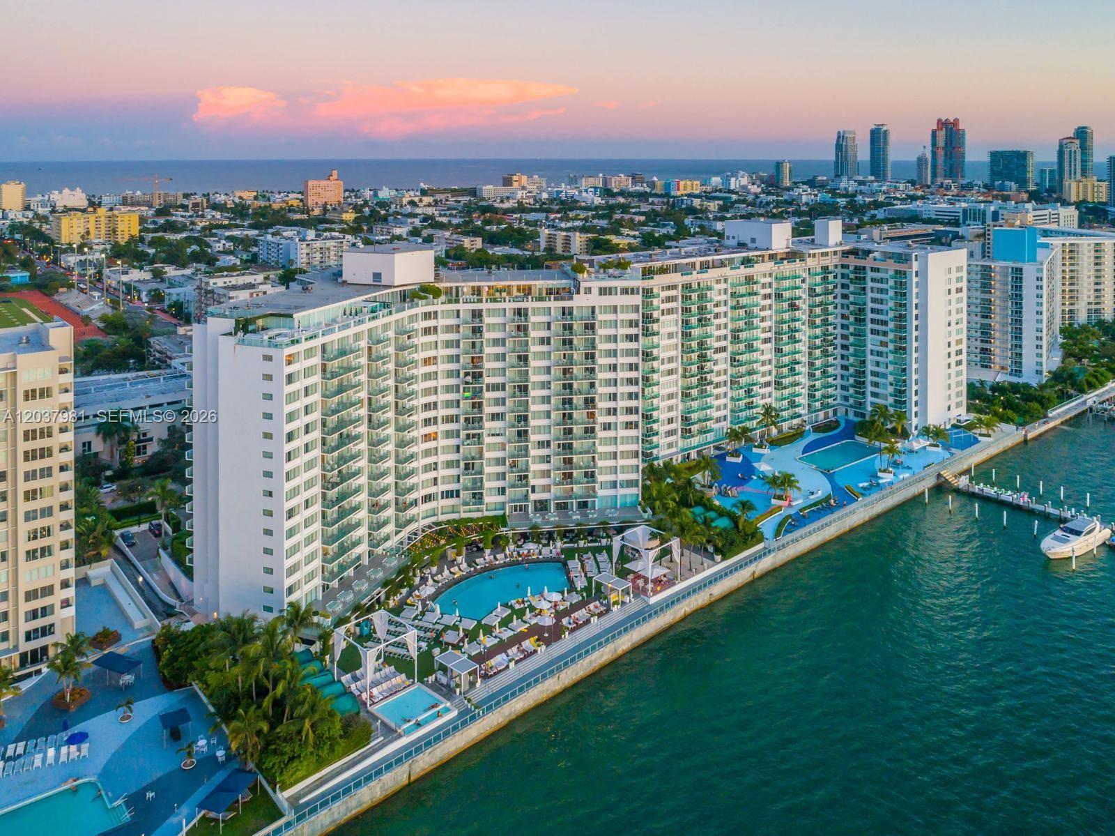 An aerial view shows a large waterfront apartment building with multiple pools and a dock — 1100 West Ave # 1012, Miami Beach FL 33139, MIAMI BEACH, FL