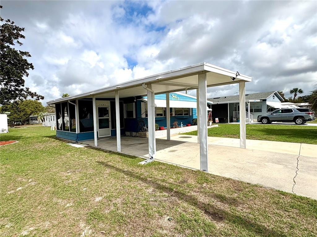 A blue mobile home features a large attached carport and a screened-in porch area — 7481 FIRST CIRCLE DRIVE, BROOKSVILLE, FL