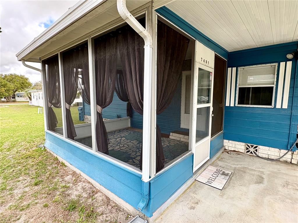 A blue house features a screened-in porch with dark curtains and a concrete entryway — 7481 FIRST CIRCLE DRIVE, BROOKSVILLE, FL