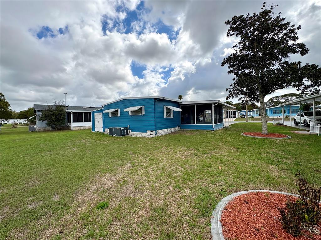 A blue mobile home with a screened porch sits on a grassy lot under clouds — 7481 FIRST CIRCLE DRIVE, BROOKSVILLE, FL
