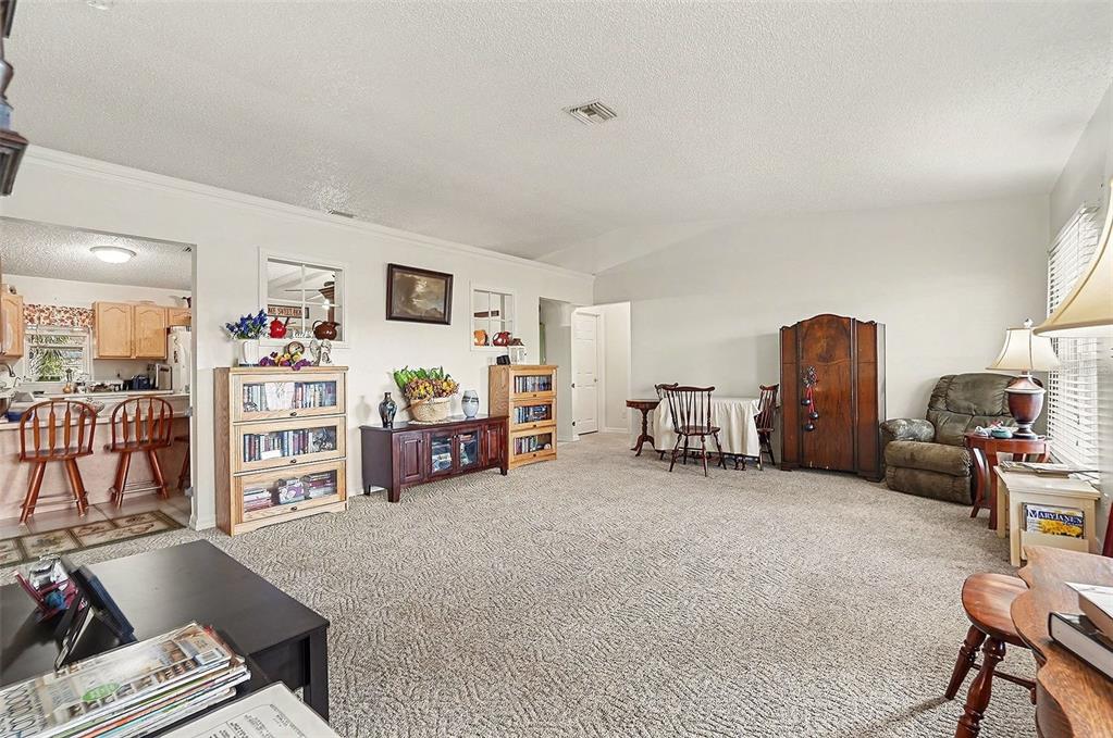 A carpeted living room features a dining area, wooden furniture, and an open kitchen view — 598 GANTRY STREET SW, PALM BAY, FL