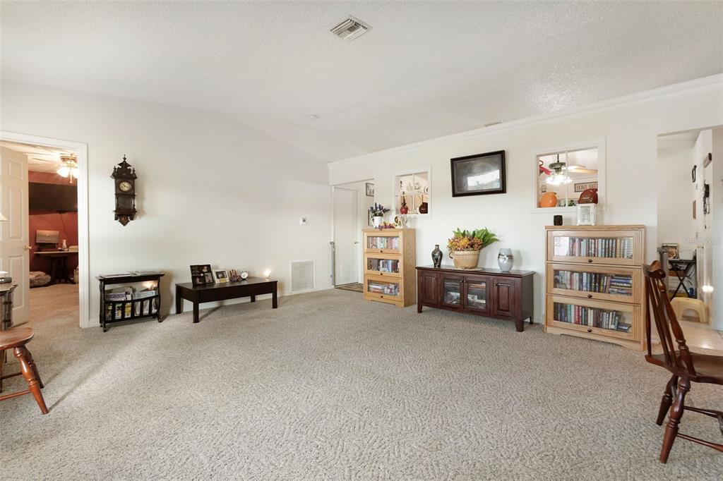 A carpeted living room features a vaulted ceiling, several wooden bookcases, and a dark console — 598 GANTRY STREET SW, PALM BAY, FL