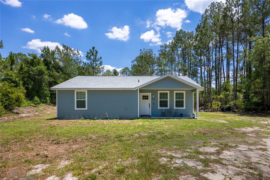 A single-story, light blue house with a gabled roof sits on a grassy lot — 9025 SE COUNTY ROAD 221, HAMPTON, FL