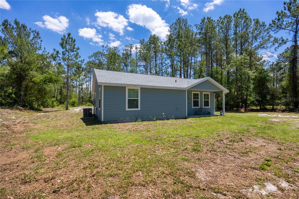 A blue-sided house with a gray roof sits on a grassy lot near trees — 9025 SE COUNTY ROAD 221, HAMPTON, FL