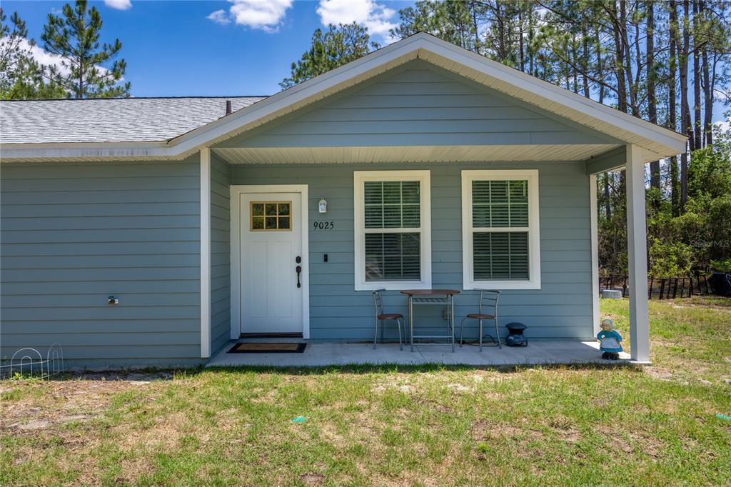 A light blue house exterior features a covered front porch with a small bistro set — 9025 SE COUNTY ROAD 221, HAMPTON, FL