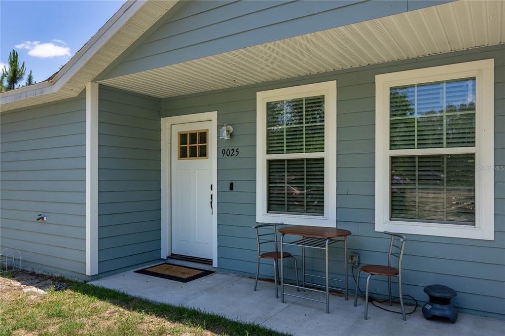 A light blue house exterior features a front door, two windows, and a small patio — 9025 SE COUNTY ROAD 221, HAMPTON, FL