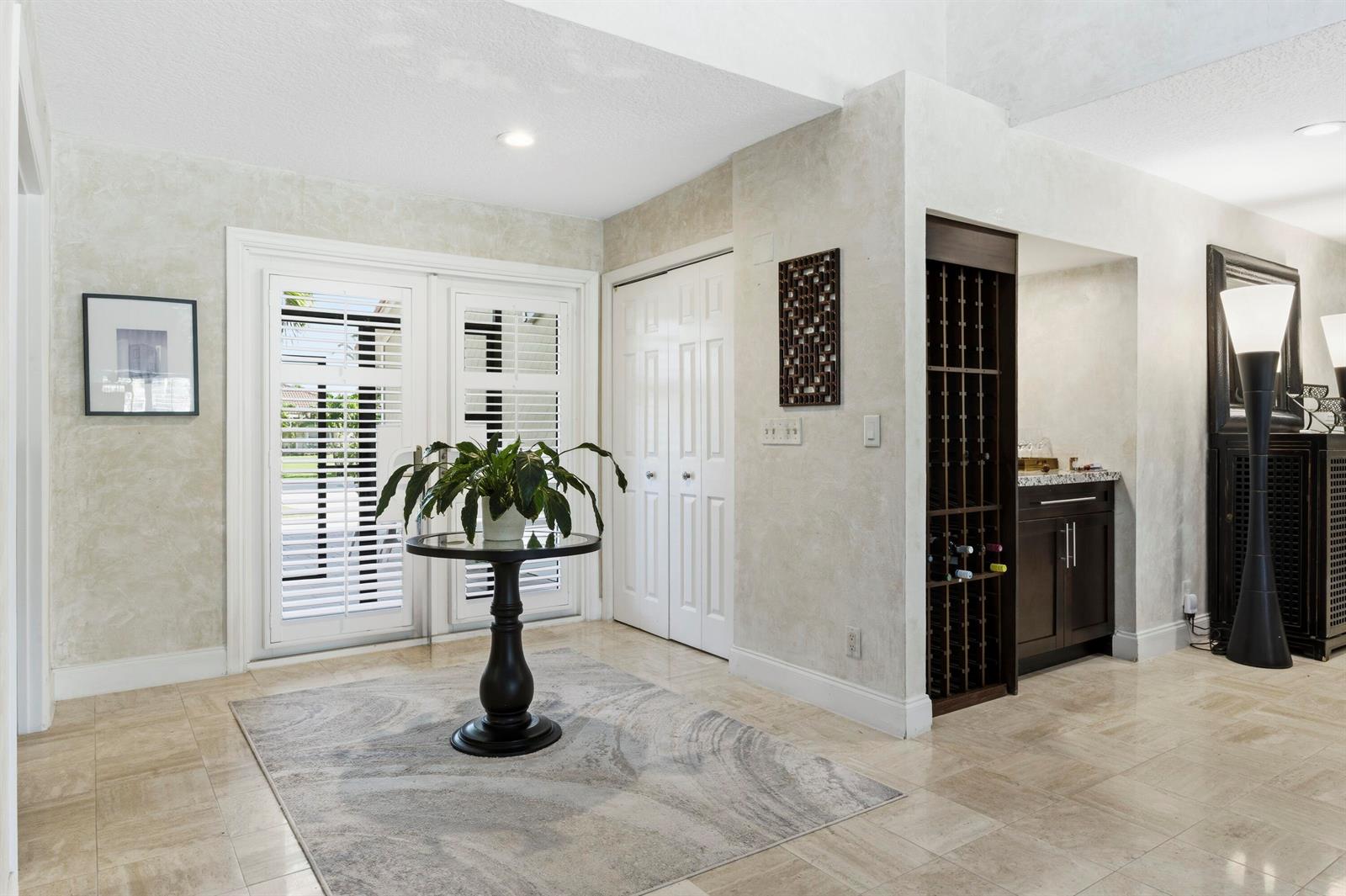 A foyer features a round pedestal table, a wine rack, and double doors with shutters — 11327 Wingfoot Drive, Boynton Beach FL 33437, BOYNTON BEACH, FL