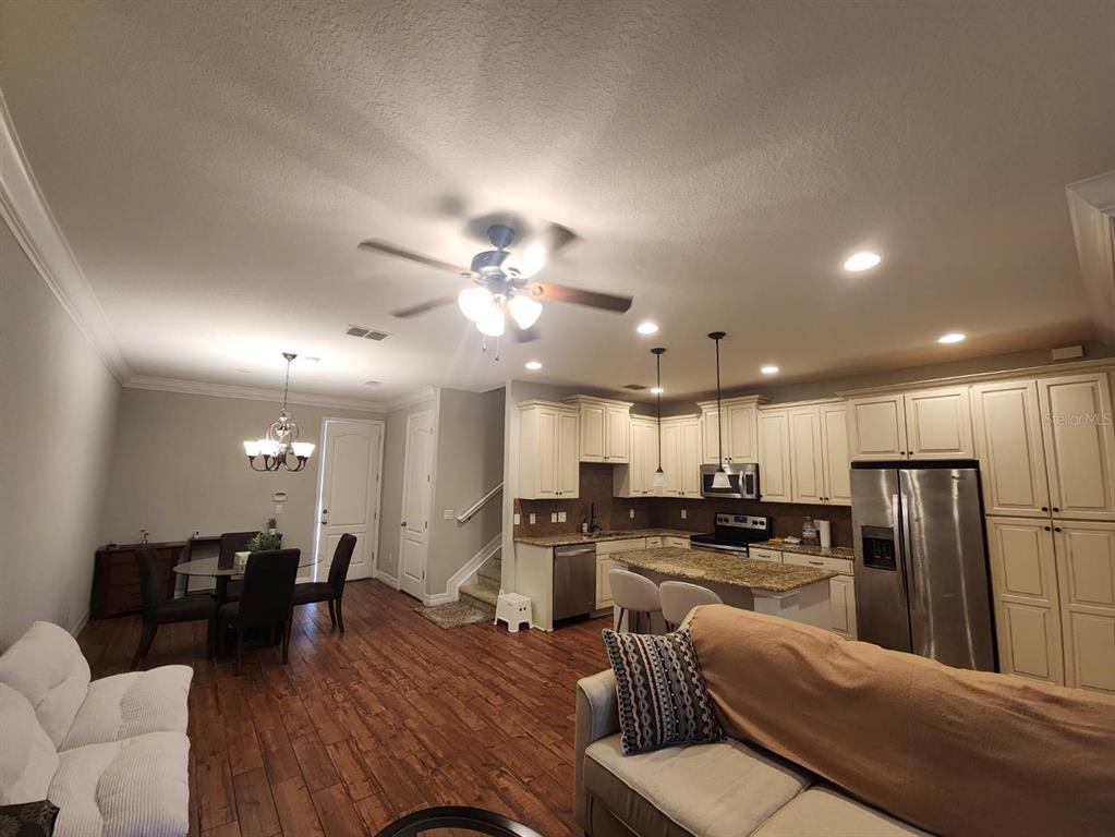 An open-concept kitchen and dining area features white cabinetry, stainless steel appliances, and wood flooring — 10052 EAGLE CREEK CENTER BOULEVARD, ORLANDO, FL