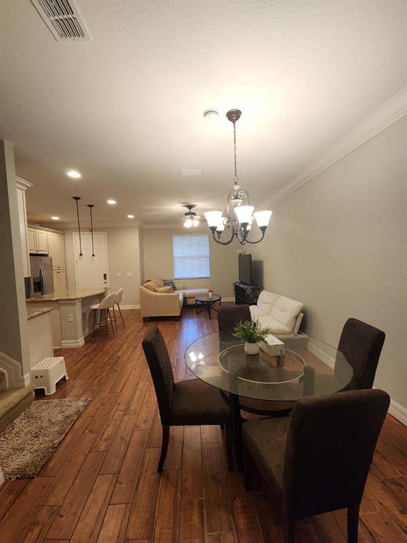 An open-concept living and dining area features wood-look flooring, a glass dining table, and kitchen — 10052 EAGLE CREEK CENTER BOULEVARD, ORLANDO, FL