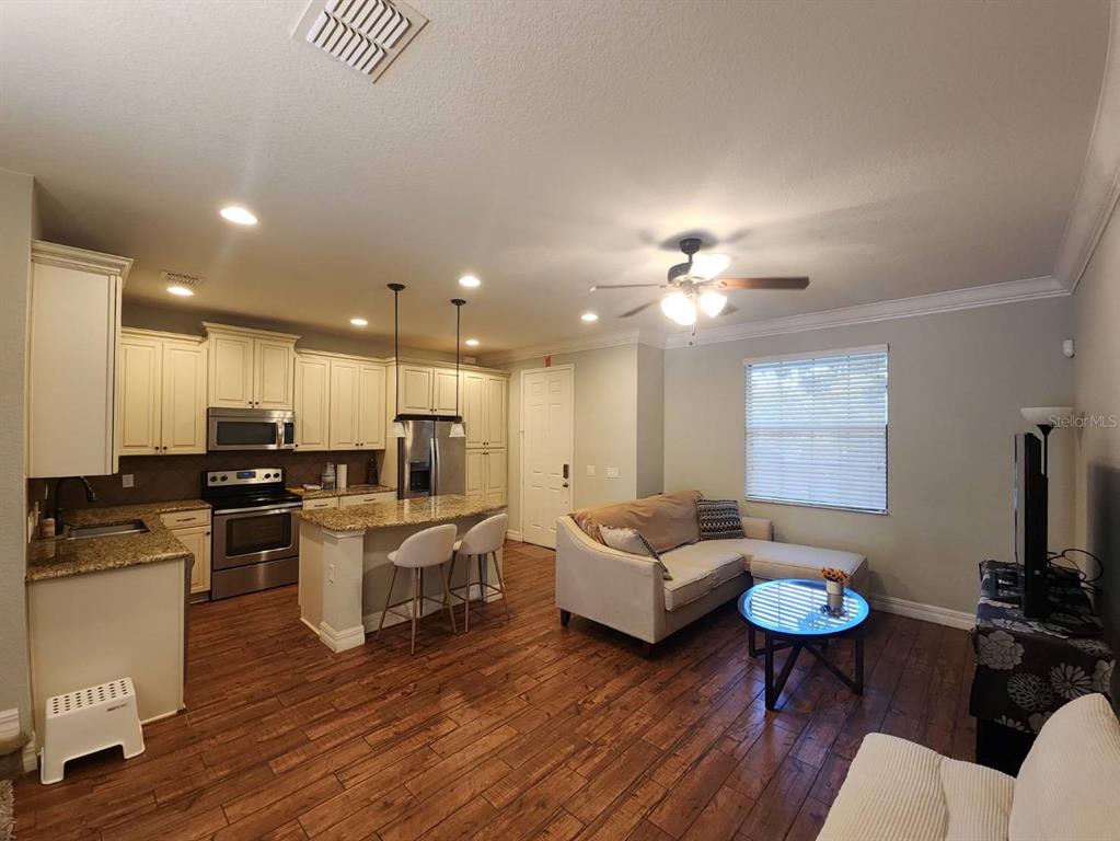 An open-concept kitchen and living room featuring wood-look flooring, granite countertops, and white cabinetry — 10052 EAGLE CREEK CENTER BOULEVARD, ORLANDO, FL