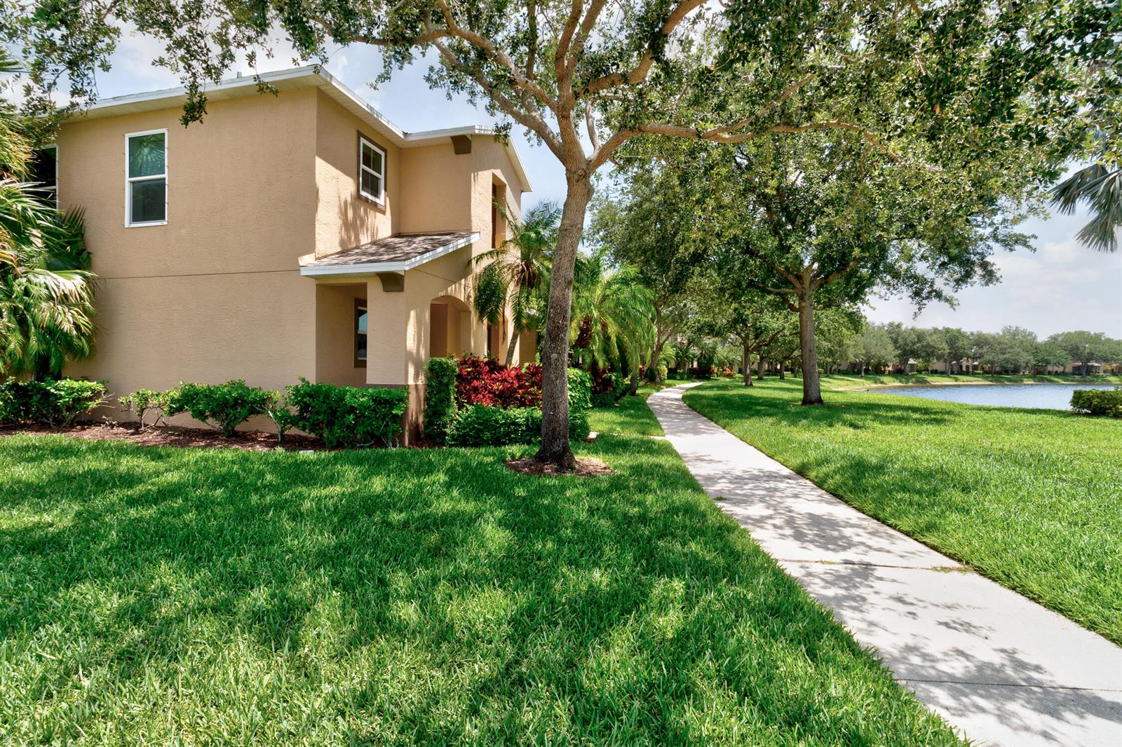 A tan two-story building sits beside a paved walkway, green lawn, and a small lake — 1670 Pointe West Way # 1670, Vero Beach FL 32966, VERO BEACH, FL