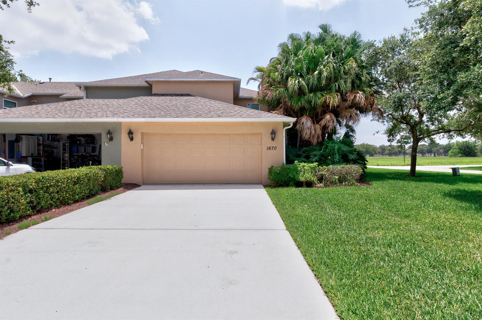 A beige house exterior features a two-car garage, a concrete driveway, and a palm tree — 1670 Pointe West Way # 1670, Vero Beach FL 32966, VERO BEACH, FL