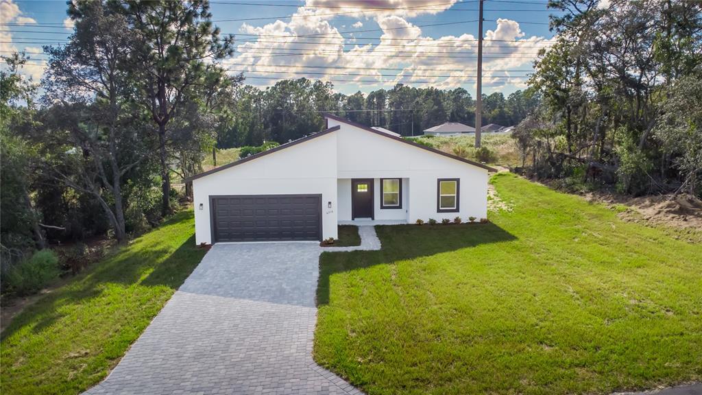 A modern single-story house with a white exterior, dark garage door, and a paved driveway — 6216 SW 155TH STREET ROAD, OCALA, FL