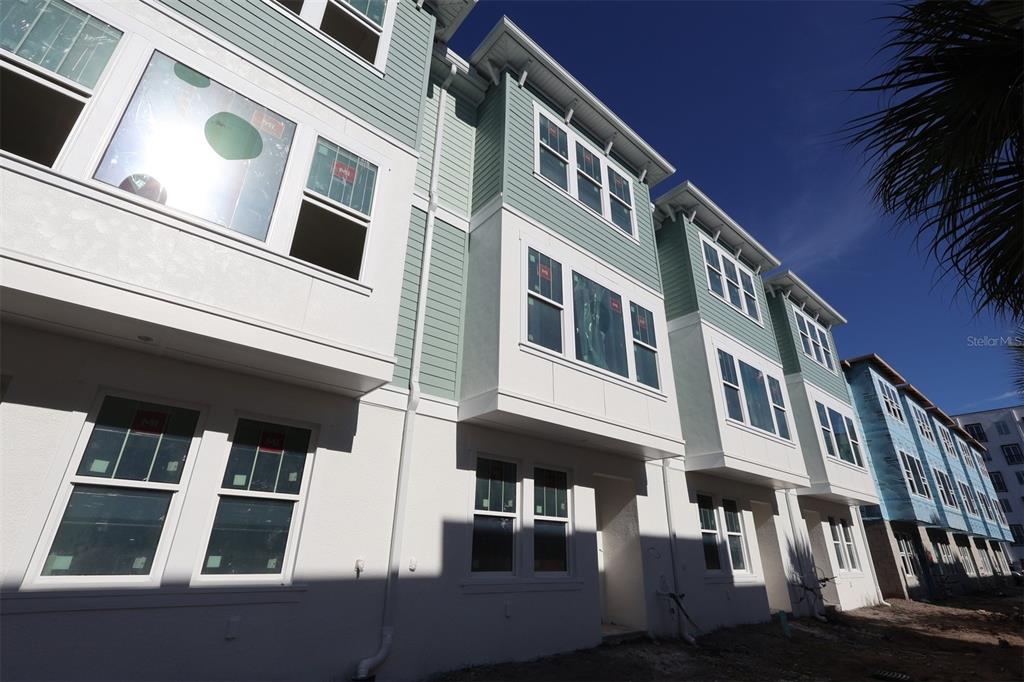 A low-angle exterior view of a multi-story townhouse complex with light green siding and white trim — 470 31ST WAY N, ST PETERSBURG, FL