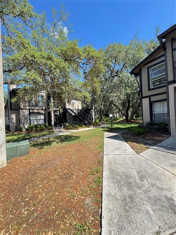 A concrete walkway leads between two multi-story apartment buildings surrounded by large, mature trees — 4033 DREAM OAK PLACE UNIT 101, TAMPA, FL
