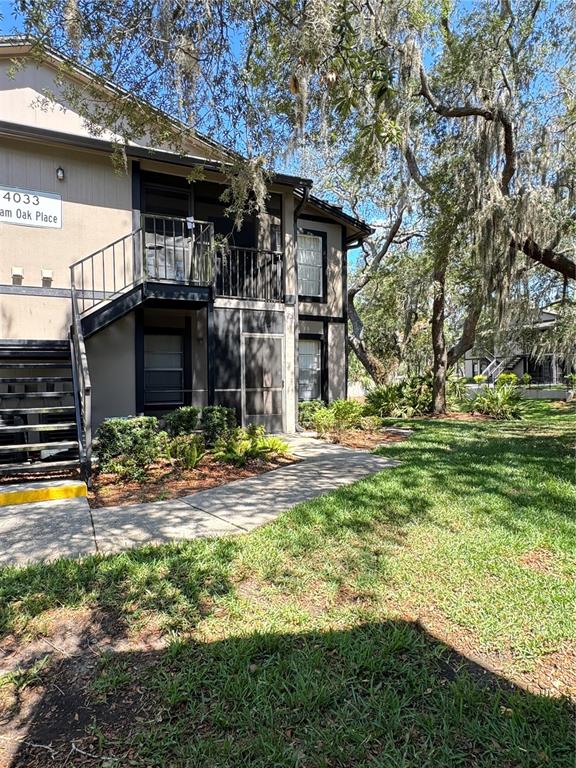 A two-story apartment building exterior features a metal staircase, screened balconies, and surrounding trees — 4033 DREAM OAK PLACE UNIT 101, TAMPA, FL