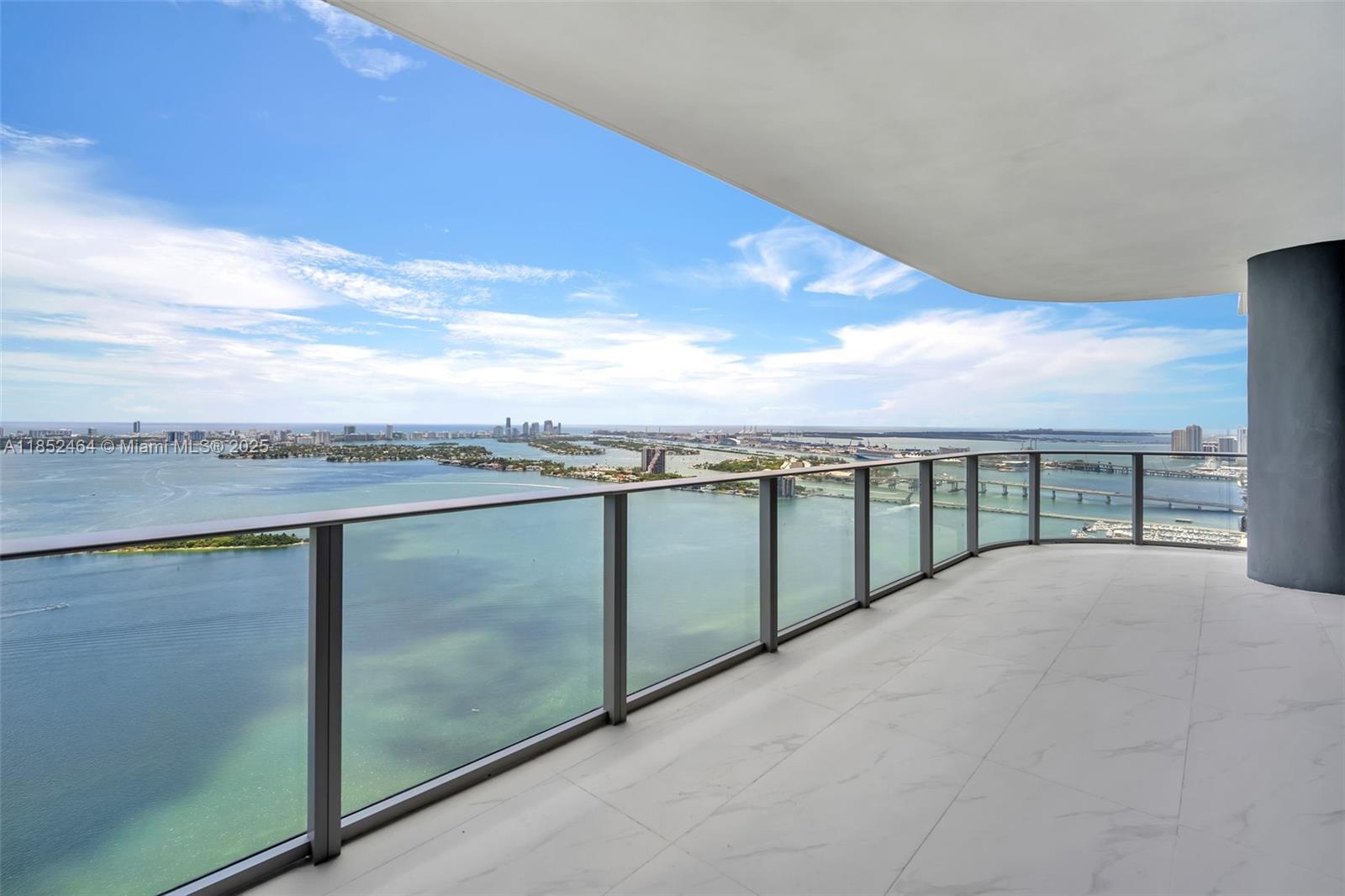 A high-rise balcony features glass railings, white marble-look tile flooring, and panoramic bay views — 700 Ne 24th St # 4507, Miami FL 33137, MIAMI, FL