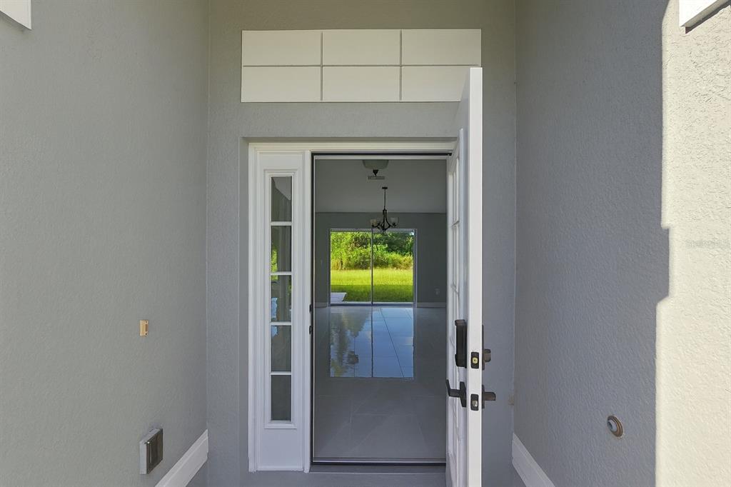 A view through an open front door into a bright, tiled home with backyard scenery — 116 RIDGEMONT DRIVE, LEHIGH ACRES, FL