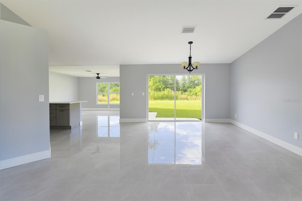 A bright, open-concept living area with light gray walls, large tile flooring, and sliding doors — 116 RIDGEMONT DRIVE, LEHIGH ACRES, FL