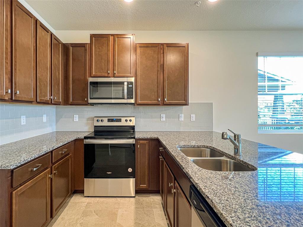 A kitchen features brown cabinets, granite countertops, stainless steel appliances, and a light-colored tile backsplash — 10227 HIGHLINE CREST STREET, ORLANDO, FL