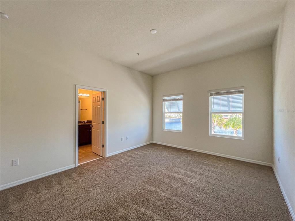 A bedroom with beige walls, brown carpet, two windows, and an open door to a bathroom — 10227 HIGHLINE CREST STREET, ORLANDO, FL