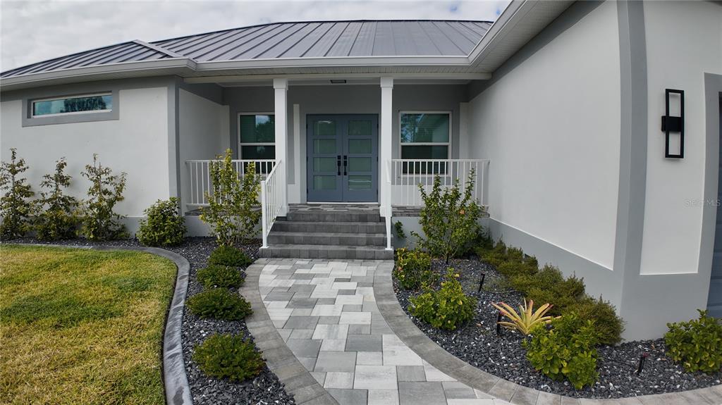 A paved walkway leads to the front entrance of a house with a metal roof — 1222 UNDERHILL CIRCLE, PORT CHARLOTTE, FL