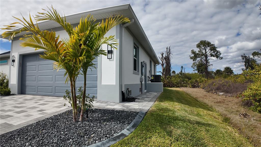 A side view of a house exterior featuring a garage, paver driveway, and palm tree — 1222 UNDERHILL CIRCLE, PORT CHARLOTTE, FL