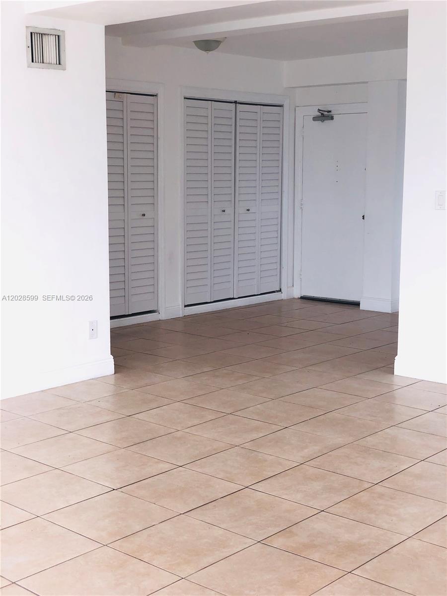 A room with white walls, tiled flooring, two sets of louvered closet doors, and an entrance — 1430 Brickell Bay Dr # 5, Miami FL 33131, MIAMI, FL