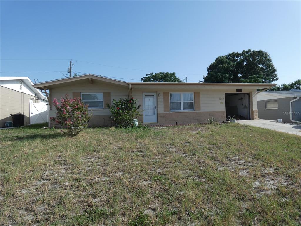 A single-story house with a beige exterior, a front-facing garage, and a dry grass lawn — 5052 CICERO DRIVE, NEW PORT RICHEY, FL