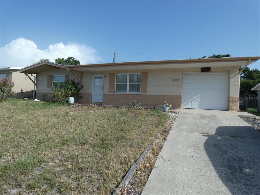 A single-story house with a beige exterior, a front-facing garage, and a concrete driveway — 5052 CICERO DRIVE, NEW PORT RICHEY, FL