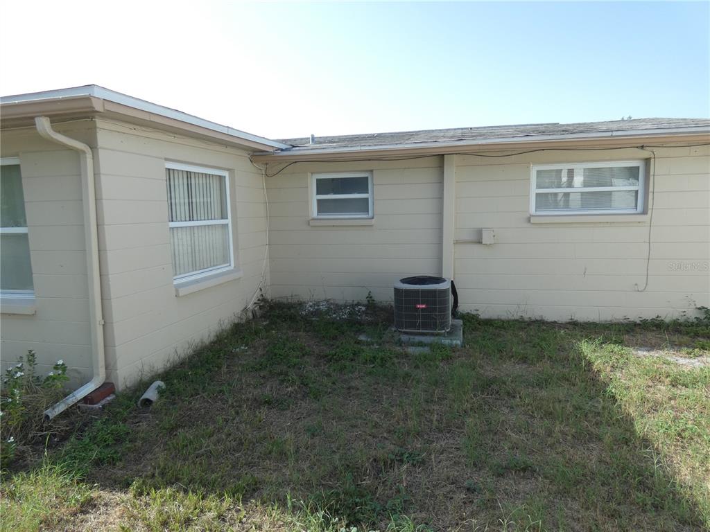 The exterior of a beige concrete block house features an air conditioning unit and windows — 5052 CICERO DRIVE, NEW PORT RICHEY, FL