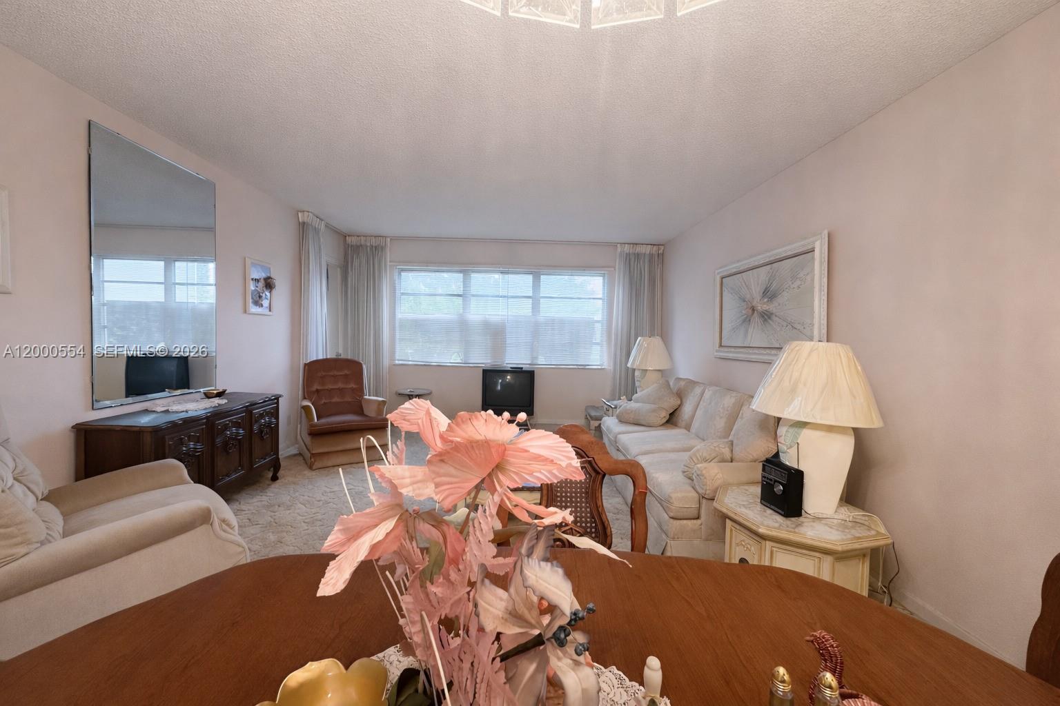 A living room features a beige sofa, a wooden sideboard, and a large wall mirror — 410 SE 2nd St # 305, Hallandale Beach FL 33009, HALLANDALE BEACH, FL