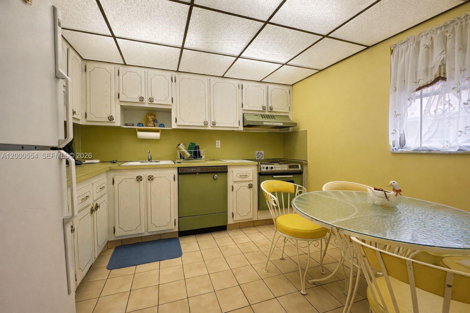 A kitchen features white cabinets, green appliances, yellow walls, and a glass-topped dining table — 410 SE 2nd St # 305, Hallandale Beach FL 33009, HALLANDALE BEACH, FL
