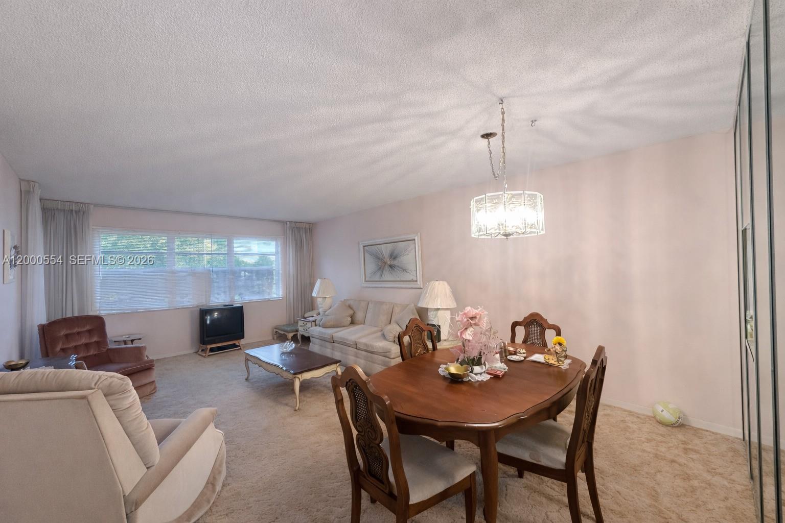 A carpeted living and dining room features a wooden table, sofa, and chandelier — 410 SE 2nd St # 305, Hallandale Beach FL 33009, HALLANDALE BEACH, FL