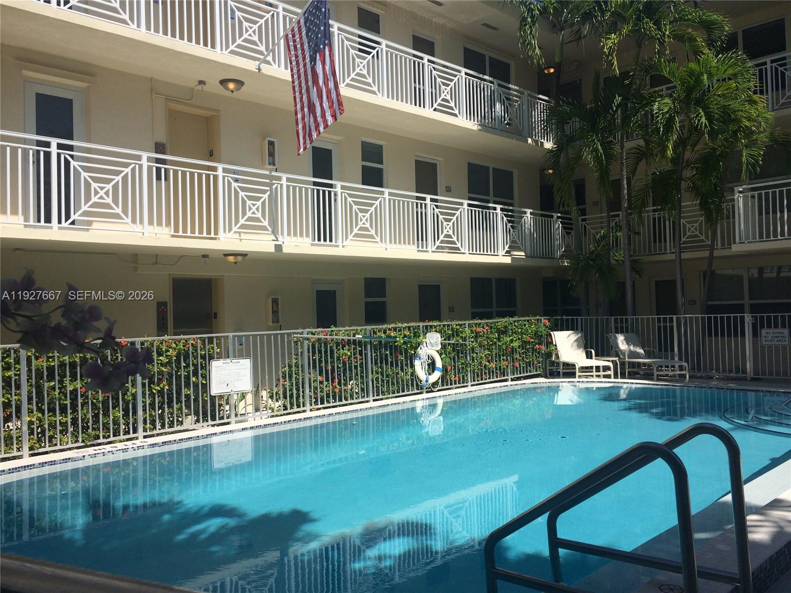 A swimming pool sits in front of a multi-story apartment building with white balconies — 255 Sunrise Dr # 103, Key Biscayne FL 33149, KEY BISCAYNE, FL
