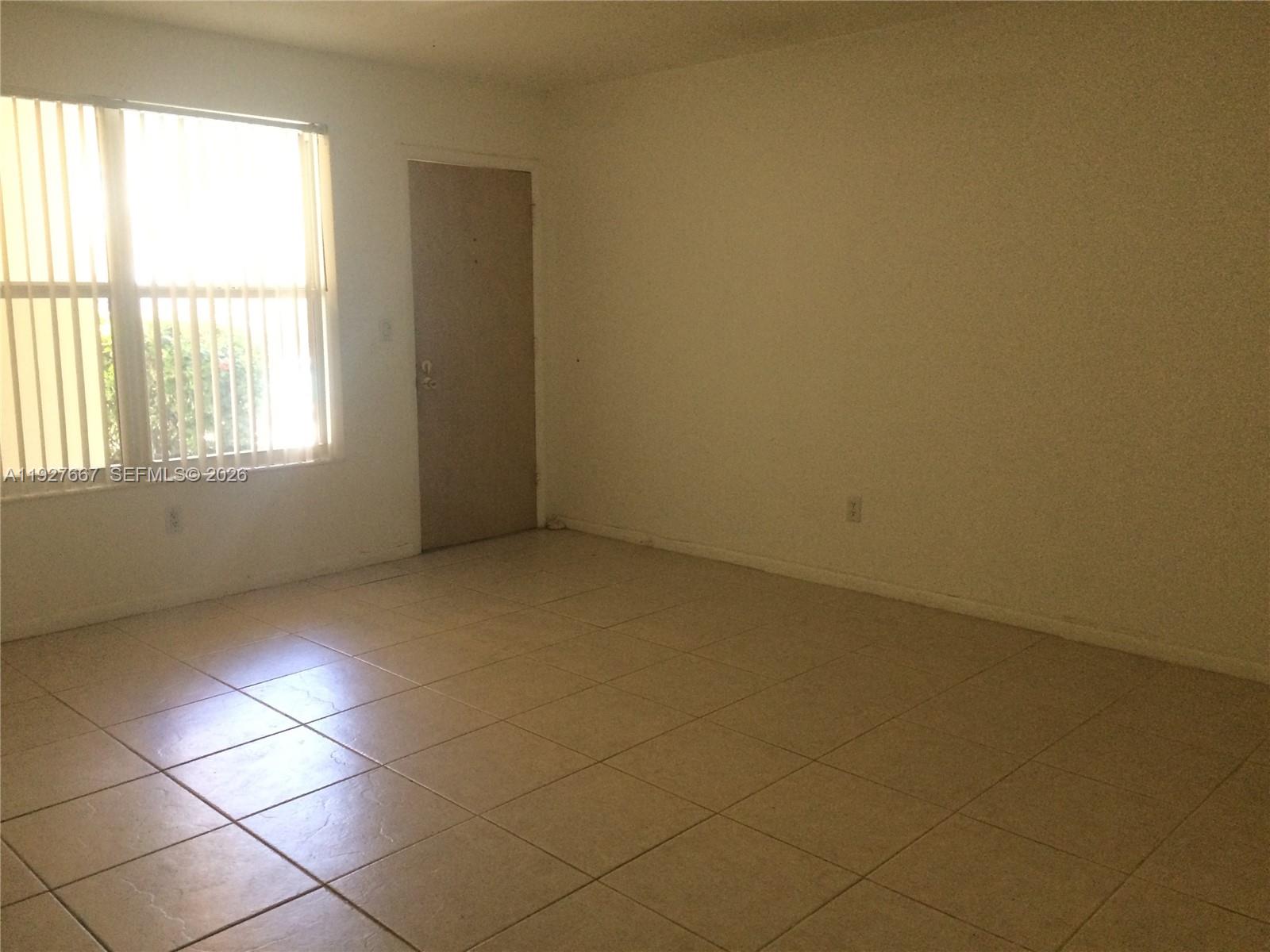 An empty room features beige tile flooring, white walls, and a window with vertical blinds — 255 Sunrise Dr # 103, Key Biscayne FL 33149, KEY BISCAYNE, FL