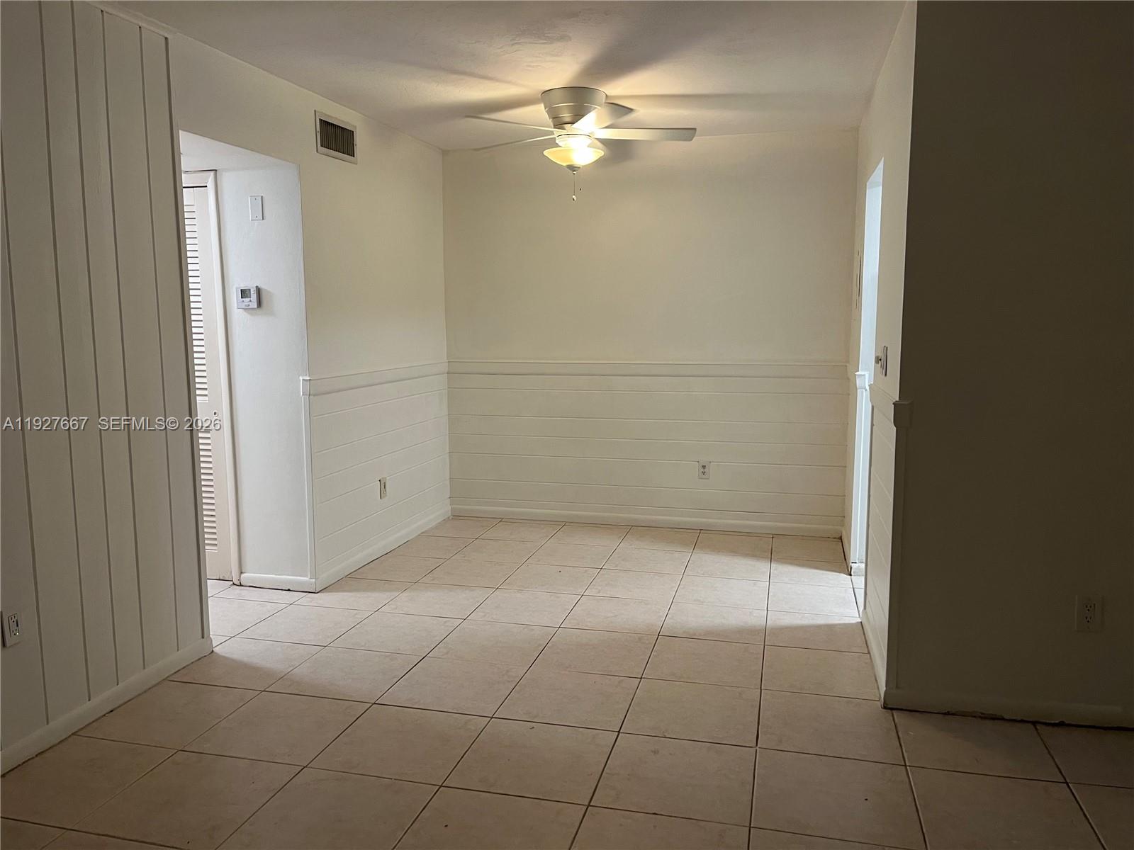 An empty room features white horizontal wall paneling, light-colored tile flooring, and a ceiling fan — 255 Sunrise Dr # 103, Key Biscayne FL 33149, KEY BISCAYNE, FL