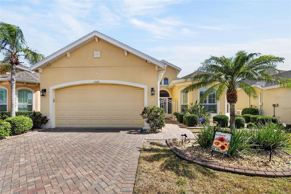 A single-story house with a beige stucco exterior, a two-car garage, and a brick driveway — 1525 EMERALD DUNES DRIVE, SUN CITY CENTER, FL