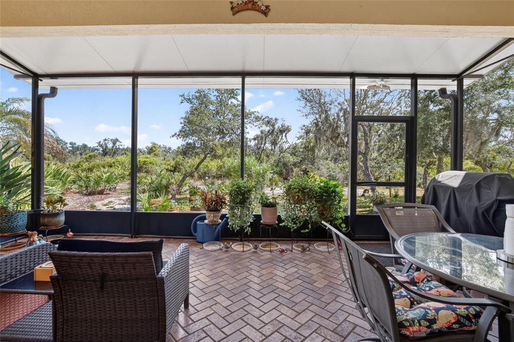 A screened-in patio features brick flooring, outdoor furniture, and a view of natural landscaping — 1525 EMERALD DUNES DRIVE, SUN CITY CENTER, FL